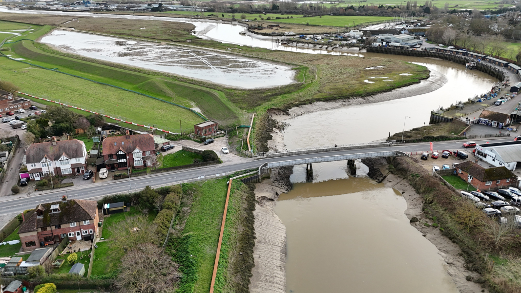 River running under a bridge next to fields.
