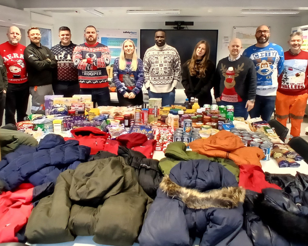 7Men and women stood in front of a table with clothing on all wearing Christmas jumpers