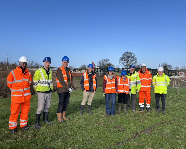 Group of men and women in Hi-vis workwear stood in a field with blue skies