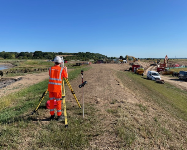 Construction worker in orange hi-vis workwear stood on a field operating equipment