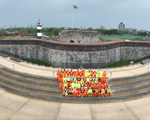 Group of men and women in hi-vis orange and yellow workwear stood on steps in front of Southsea Castle
