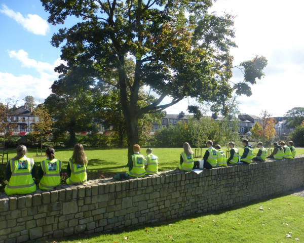 Group of school students in hi-vis sat on a wall looking out towards a field