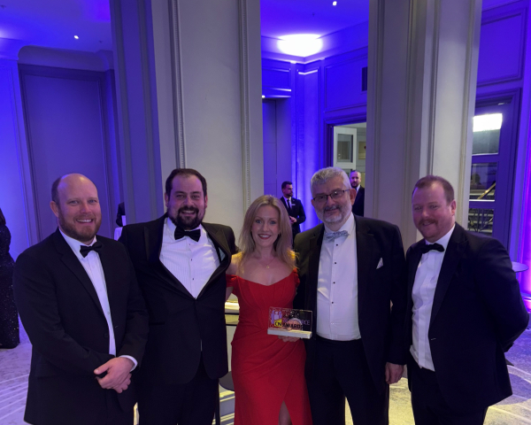 four men in black tie and one women in a red dress stood together with a glass trophy
