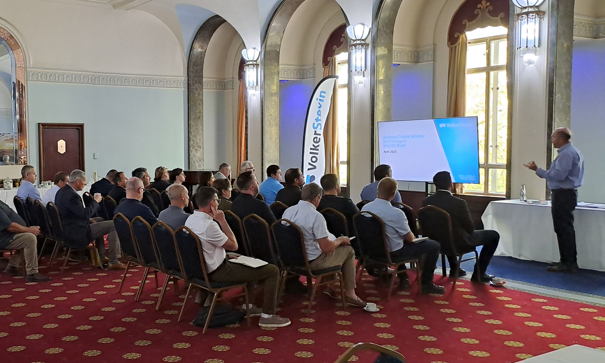 Room of people sat being presented to with slides on a large screen